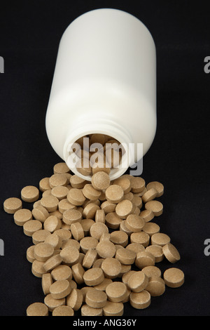 Plain white bottle on it's side spilling thick round mottled brown tablets in large pool before it Stock Photo