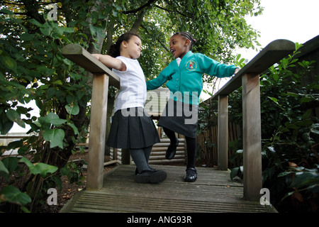 A white and an Afro Caribbean girl chat on a foot bridge in the grounds of a nursery school in the West Midlands UK Stock Photo