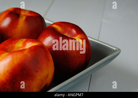 Nectarines in ceramic bowl on blue wooden table Stock Photo