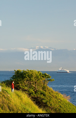 A woman enjoying the view along the Dallas Road waterfront as the Coho Ferry passes in the distance in Victoria, Vancouver Islan Stock Photo