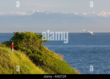 A woman enjoying the view along the Dallas Road waterfront as the Coho Ferry passes in the distance in Victoria, Vancouver Islan Stock Photo