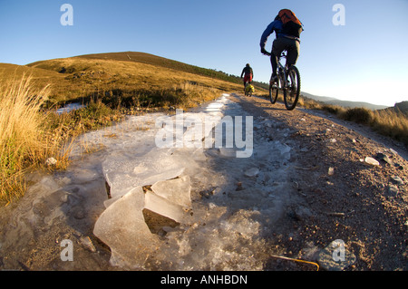 Mountain bikers ride in the Cairngorms National Park on a glorious clear winters day. Carrying all the gear for an overnight. Stock Photo