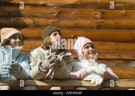 Three preteen or teen girls standing on deck of log cabin, looking away, low angle view Stock Photo