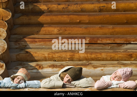 Three preteen or teen girls standing on deck of log cabin, resting heads on railing Stock Photo