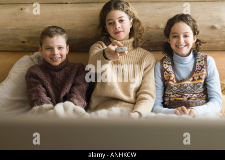 Teen girl and younger boy and girl watching TV together, front view Stock Photo