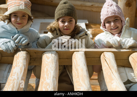 Three preteen or teen girls standing on deck of log cabin, looking down at camera, low angle view Stock Photo