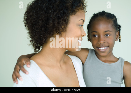 Mother holding daughter, both smiling and looking away, close-up Stock Photo
