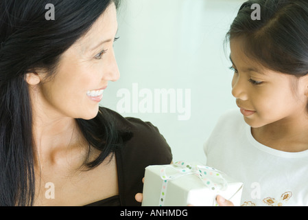 Mother and daughter smiling together, girl holding gift Stock Photo