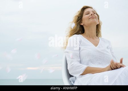 Woman sitting with head back and eyes closed among floating flower petals Stock Photo