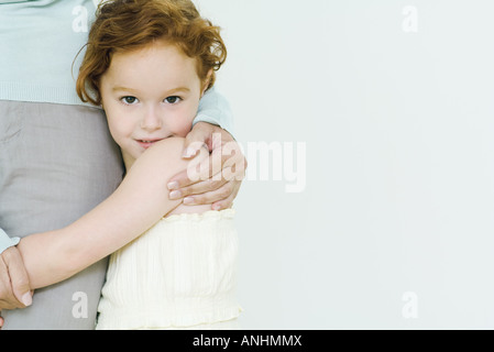 Little girl hugging mother's leg, looking at camera Stock Photo