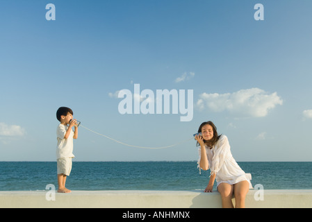 Boy speaking to woman through tin can phone, ocean horizon in background Stock Photo