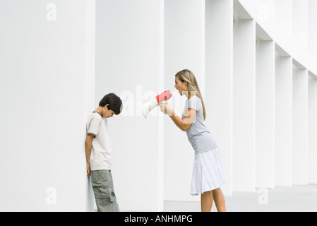 Woman shouting at boy through megaphone, boy lowering head Stock Photo