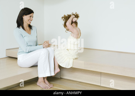 Mother and little girl, sitting together, smiling, girl holding up hair Stock Photo
