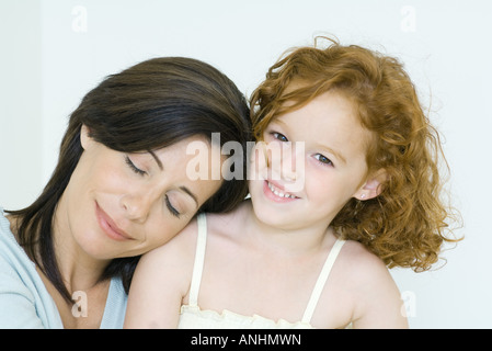 Mother and daughter, woman resting head on girl's shoulder, girl smiling at camera Stock Photo