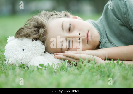Boy resting head on teddy bear, sleeping on grass Stock Photo