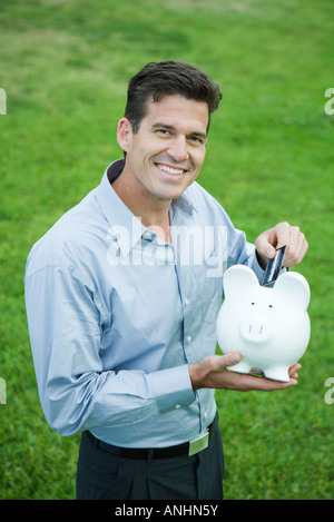 Man putting credit card into piggy bank Stock Photo