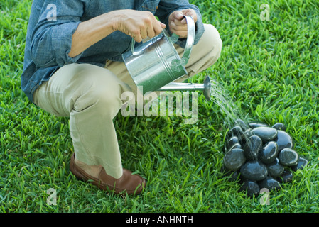 Man watering stack of pebbles, cropped Stock Photo