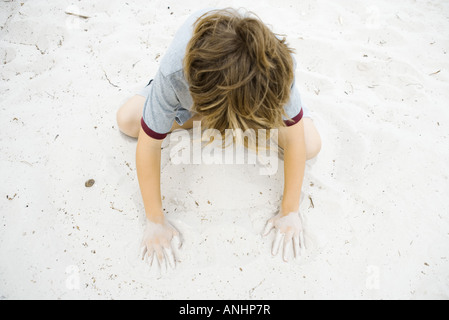 Boy crouching in sand, playing, high angle view Stock Photo