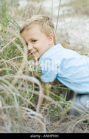 Young boy crouching in tall grass, looking over shoulder at camera