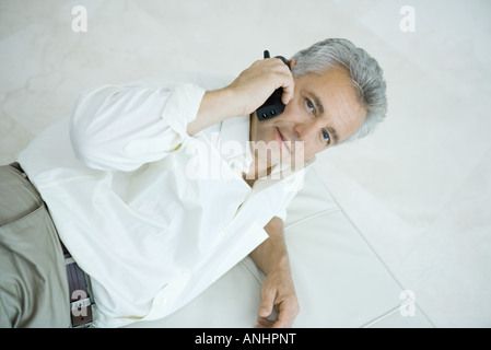 Mature man lying on side using cordless phone, looking up at camera Stock Photo