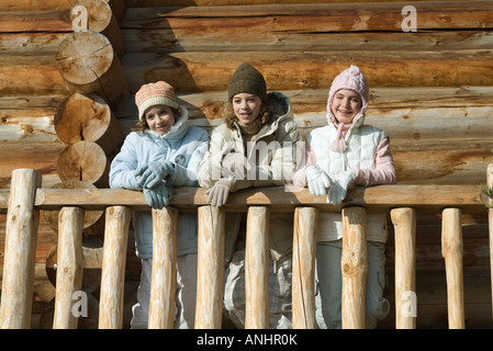Three preteen or teen girls standing on deck of log cabin, looking away, low angle view Stock Photo