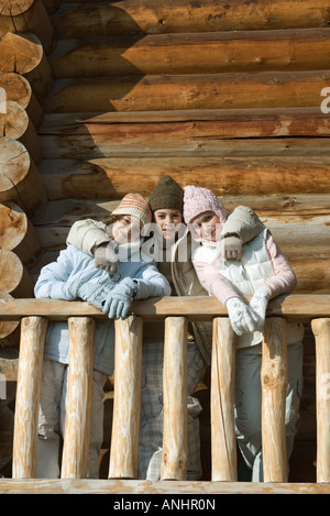 Three preteen or teen girls standing on deck of log cabin, smiling at camera Stock Photo