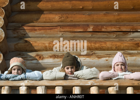 Three preteen or teen girls standing on deck of log cabin, resting heads on hands Stock Photo