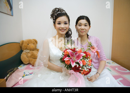 Bride sitting on bed beside bridesmaid, smiling at camera Stock Photo