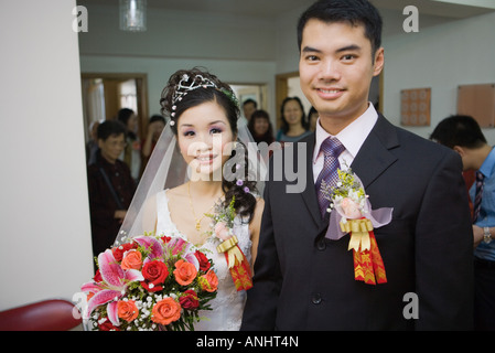 Bride and groom wearing corsages, smiling at camera, friends and family in background Stock Photo