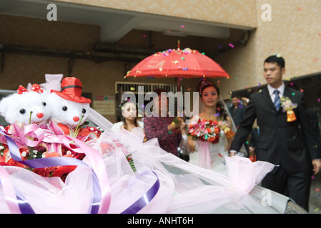 Chinese wedding, bride and groom leaving under confetti, bride covered by red parasol, decorated car in foreground Stock Photo