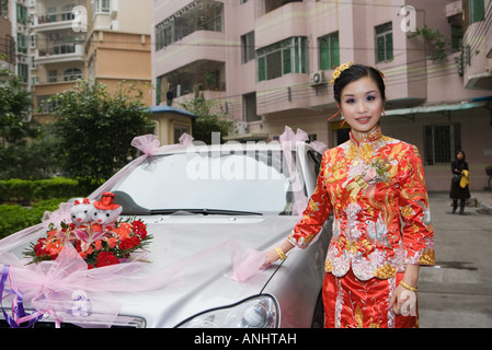 Bride dressed in traditional Chinese clothing, standing next to decorated car, smiling at camera Stock Photo