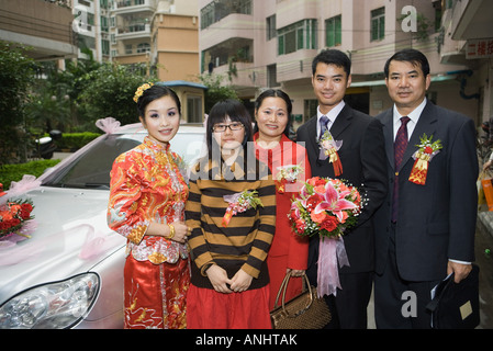 Bride and groom standing with parents and sister in front of car, portrait Stock Photo