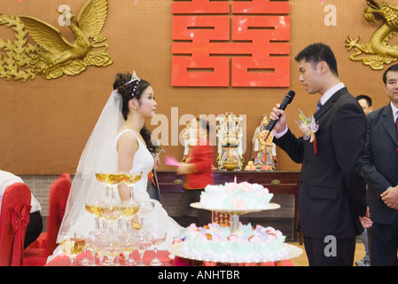 Bride and groom standing face to face, looking at each other, groom speaking into microphone Stock Photo