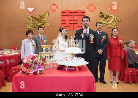 Groom standing in front of bride and parents, speaking into microphone Stock Photo