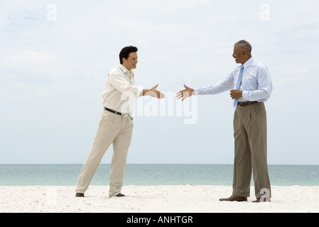 Two businessmen standing on the beach, reaching out to shake each other's hands Stock Photo