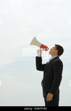 Young businessman shouting into megaphone, side view Stock Photo