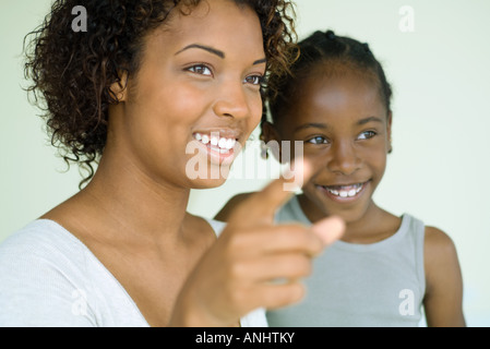 Young woman pointing finger and looking away with daughter, both smiling Stock Photo