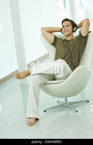 Young man listening to headphones with hands behind head, smiling, full length Stock Photo