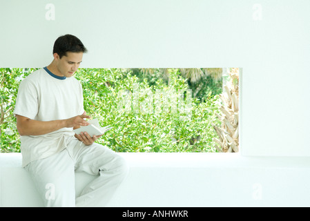 Man sitting on ledge reading book Stock Photo
