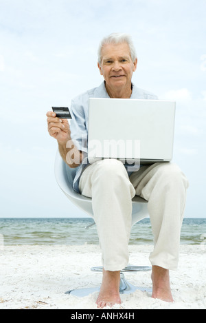 Senior man using laptop on beach, making on-line purchase with credit card Stock Photo