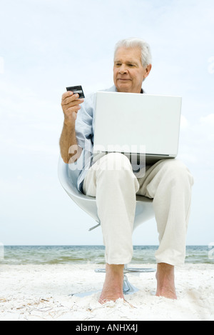 Senior man using laptop on beach, making on-line purchase with credit card Stock Photo