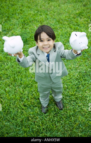 Little boy dressed in full suit holding up piggy banks Stock Photo