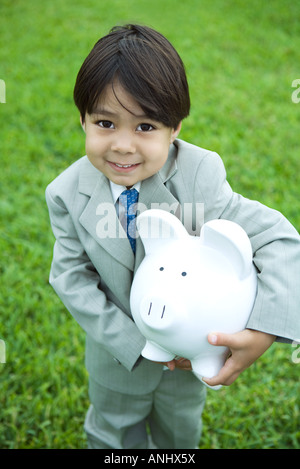 Little boy dressed in full suit holding piggy bank Stock Photo