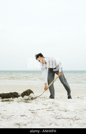 Man at the beach scooping sand with shovel, smiling at camera, full length Stock Photo