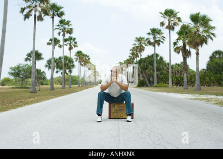 Man sitting on suitcase in the middle of street, looking away Stock Photo