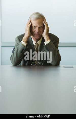 Businessman sitting with head in hands, looking at camera Stock Photo