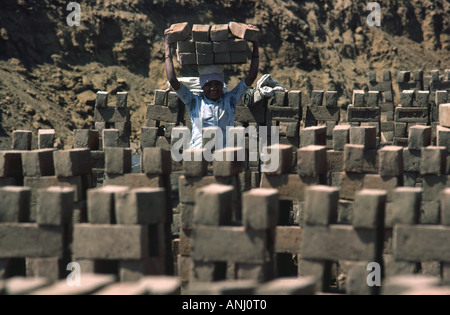 A male laborer working in a brickworks, involving the hard physical work of loading large numbers of bricks onto his head. Maharashtra, India Stock Photo