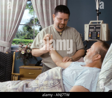 Male nurse taking pulse of elderly man patient in room Stock Photo