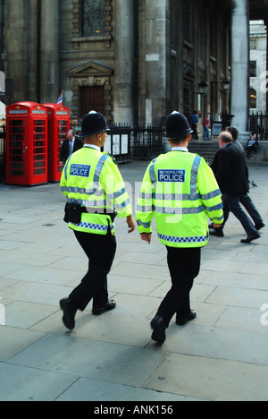 London street scene back view of two male Metropolitan police officers in uniform wearing high visibility jackets walking in step on foot patrol UK Stock Photo