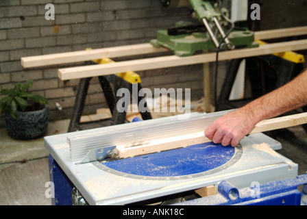 Close up Carpenters hand working with electric saw bench in driveway of domestic dwelling shaping softwood for indoors fitting in Essex England UK Stock Photo